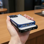 Hand holding two Motorola Edge 60 Pro 5G phone cases, one blue and one black, on a wooden surface.